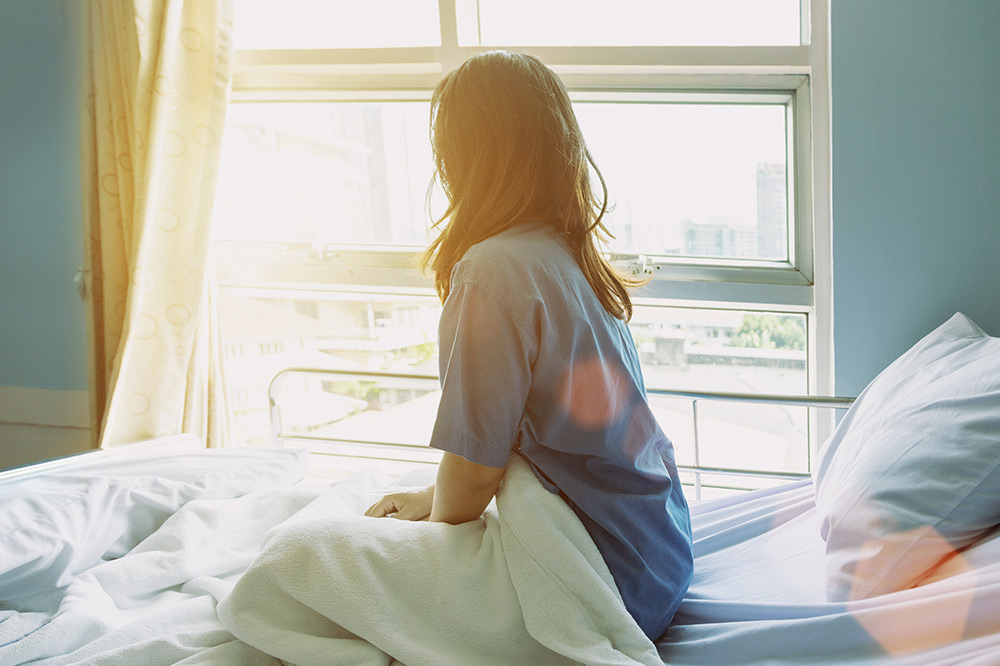 Patient contemplating the costs of lumbar disc replacement surgery while looking out a window.