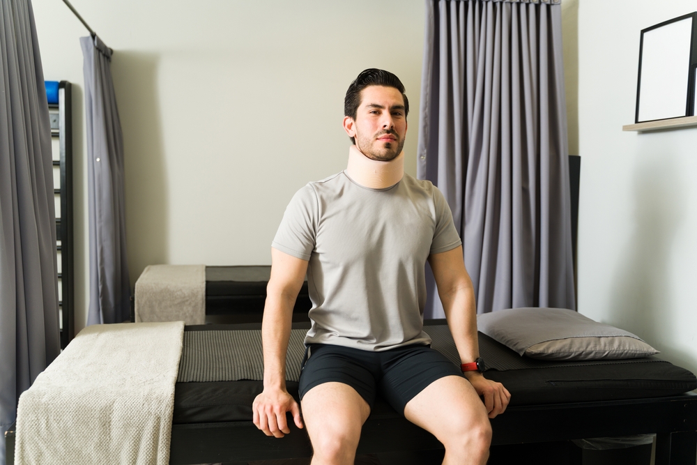 Man wearing a neck brace seated in a recovery room during early discharge period after ACDF spine surgery.