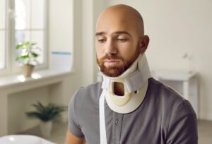 Man wearing a neck brace during cervical discectomy and fusion recovery in a bright medical consultation room.