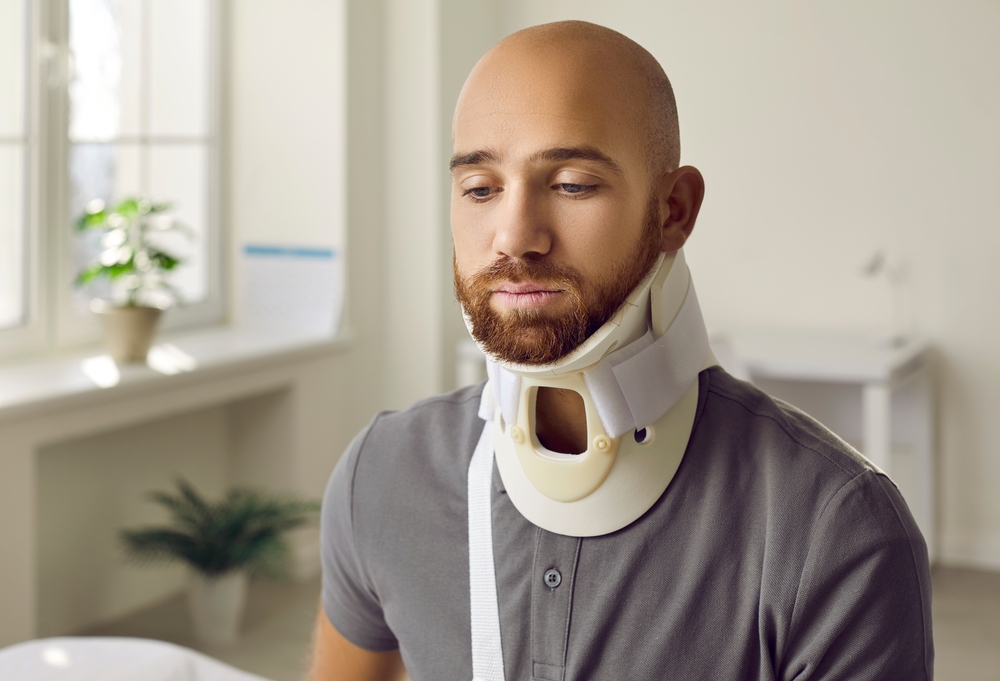 Man wearing a neck brace during cervical discectomy and fusion recovery in a bright medical consultation room.