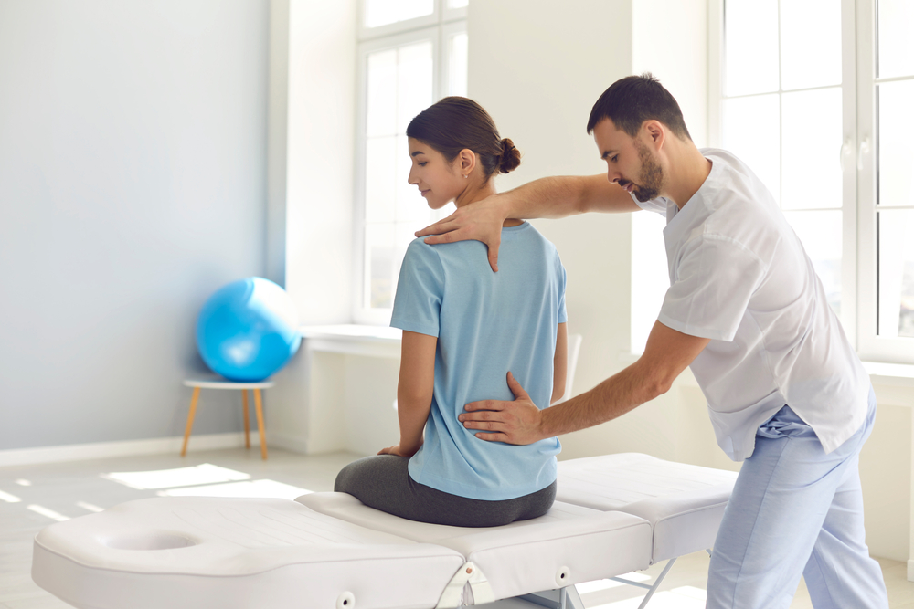 Physical therapist guiding a woman through cervical spine recovery exercises on a therapy table in a bright clinic.