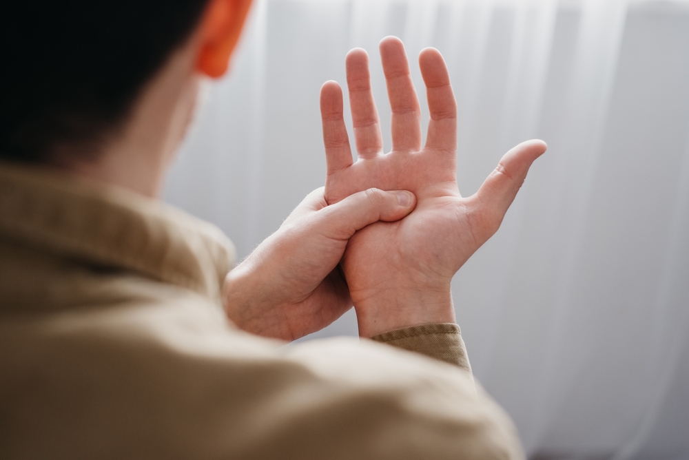 person pressing palm to relieve hand tremor possibly linked to Parkinson’s, related to deep brain stimulation therapy