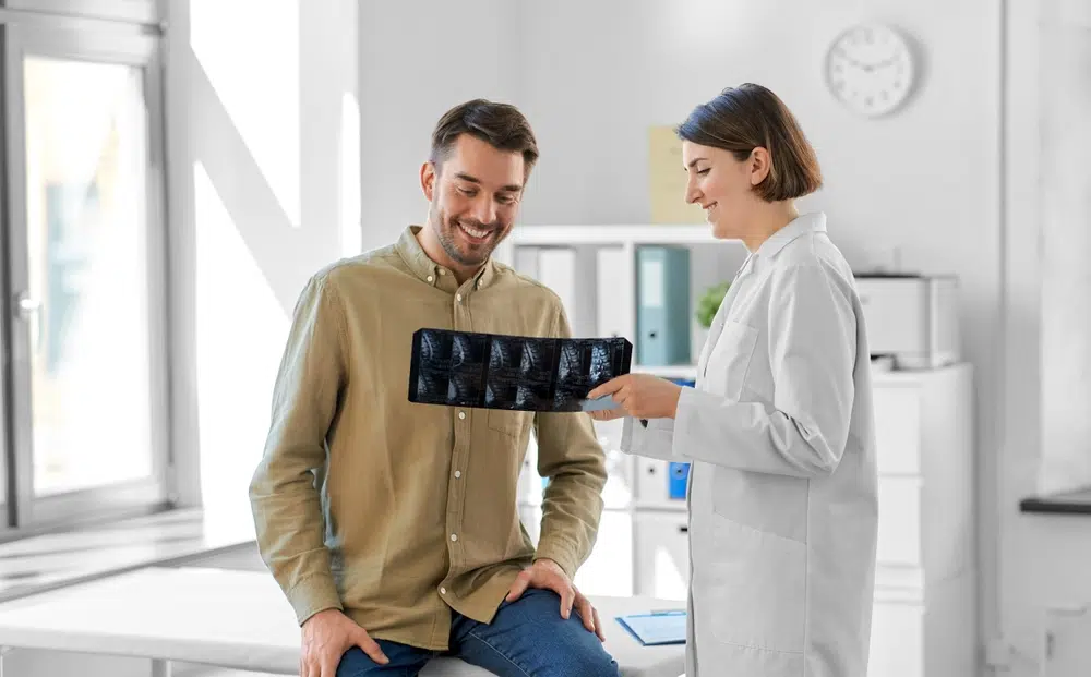 Smiling patient discussing spinal scan results with female doctor after minimally invasive spine surgery consultation.