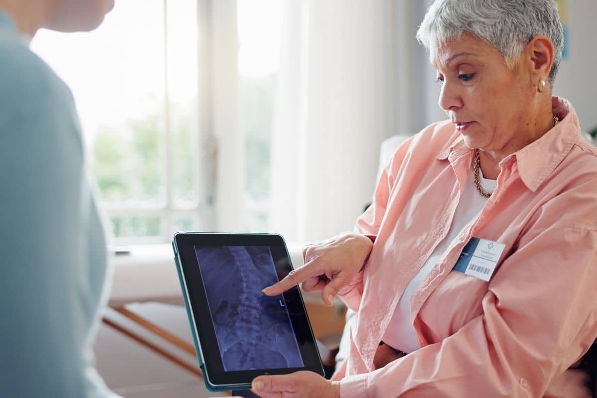 Older female patient reviewing spinal X-ray on tablet with medical specialist during early spine condition evaluation.